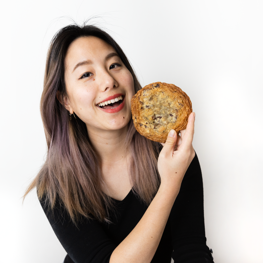 Sophia J Chang wearing a black shirt and holding a chocolate chip and cherry cookie